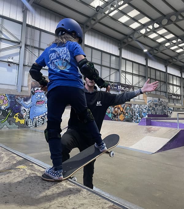 Boarding Millie learning to drop in on a ramp at a skateboard park.